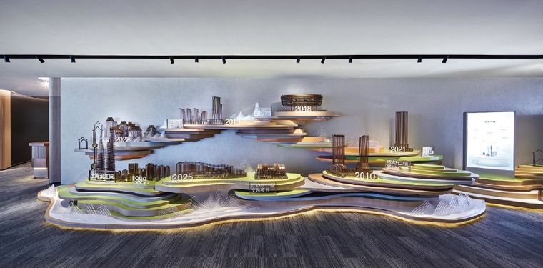 Grey exhibition hall with a circular platform, a central model and wall screens