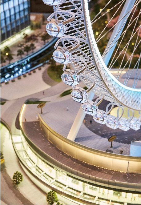 Model of a Ferris wheel above a retail building, lit at night