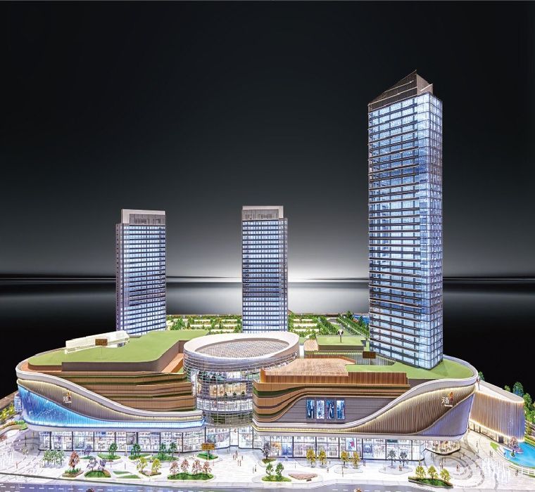 Model of three office towers above a retail podium, lit at night