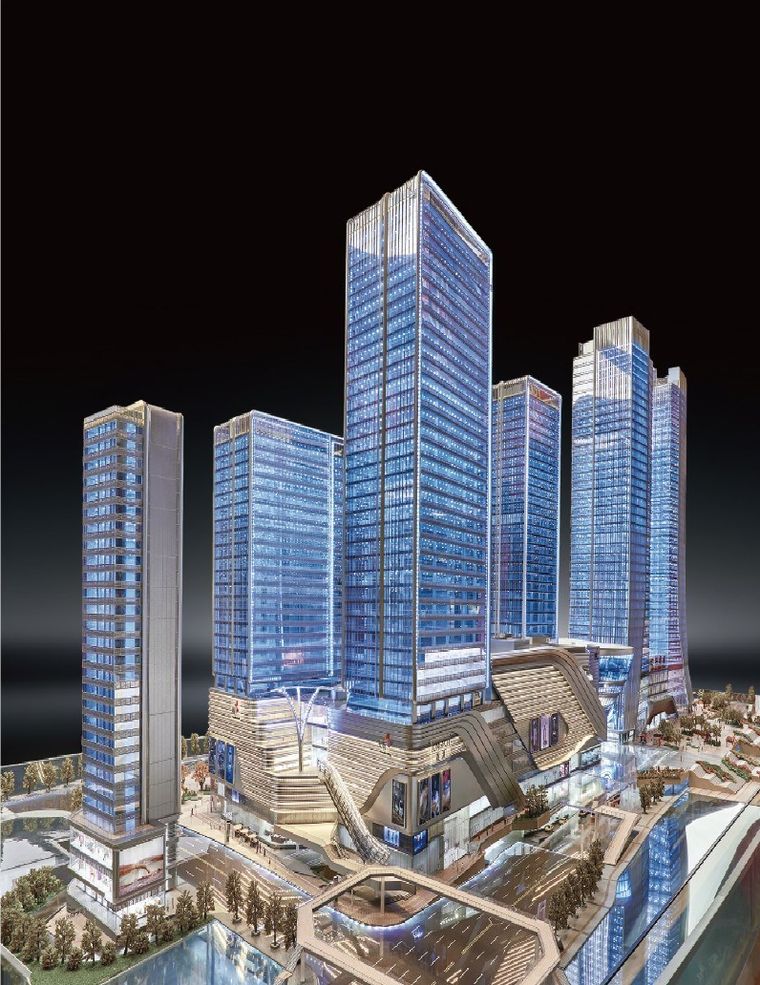 Model of a tower and retail complex lit at night against a dark background