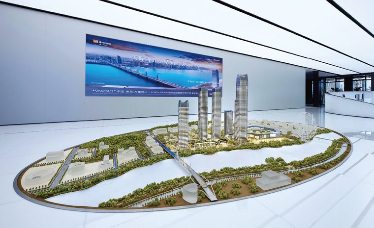 Model of a tower project on an oval base before a display panel in a white hall