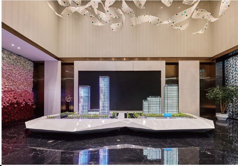 Model of a business complex in a marble lobby beside a bonsai tree