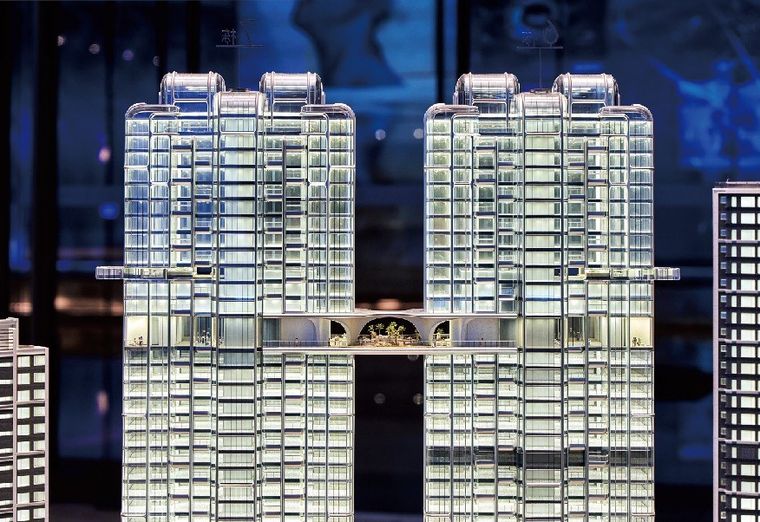 Model of two residential towers joined by a sky bridge, lit at night