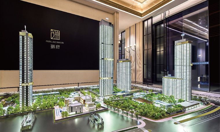 Model of a residential tower project before a wall carrying the project name