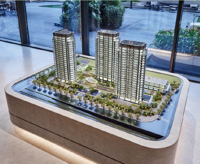 Model of two residential towers on a white base before a glazed wall