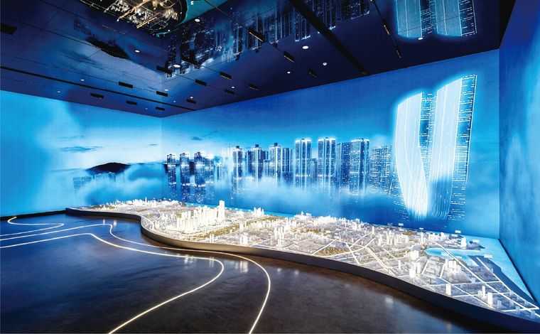 Model of a coastal city before a long blue screen wall