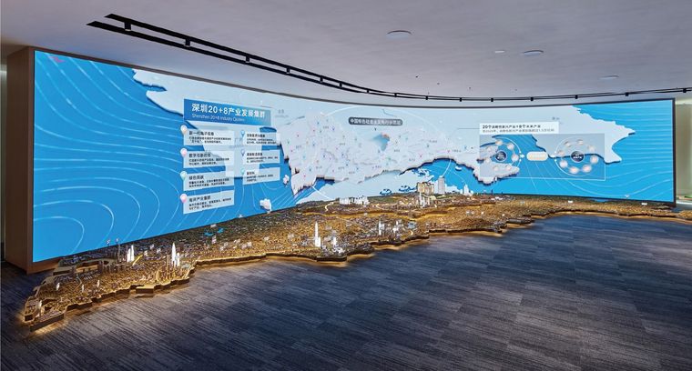 Model of an extended coastline before a blue screen showing the development map