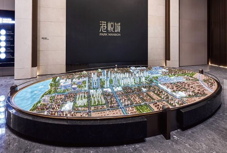 Model of a city on a circular black base before a wall carrying the project name