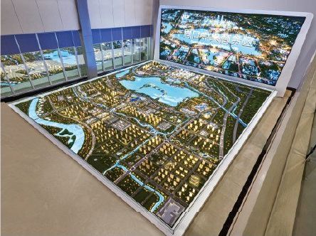 Model of a city master plan with an aerial display panel of the project