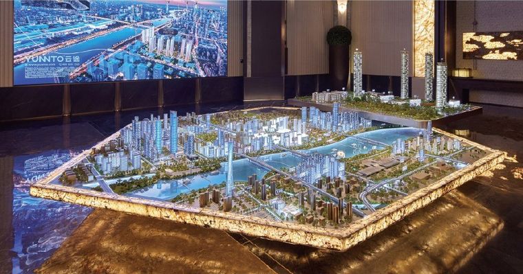 Model of a city extending through a lobby under golden light and a screen wall